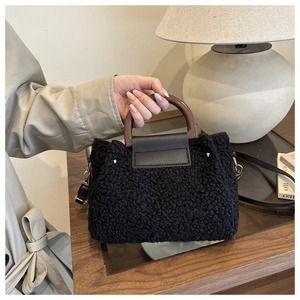 Detail of black faux shearling bucket bag with round wooden handle and leather trim