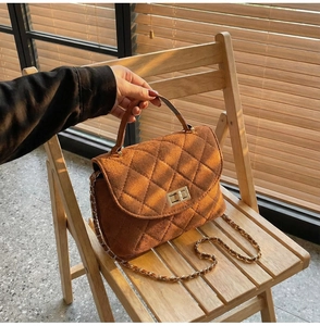 Close-up of brown quilted faux suede handbag with gold chain strap on a chair
