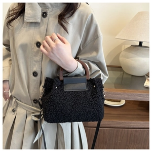 Detail of black faux shearling handbag with wooden handle and gold metal hardware