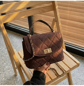 Detail of dark brown quilted suede handbag with golden metal lock and chain strap