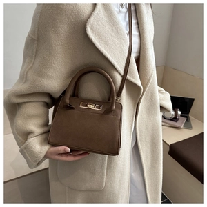 Détail du sac à main en daim marron foncé avec fermoir doré porté sur un manteau