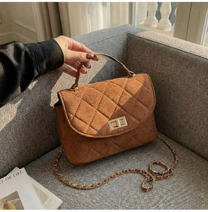 Detail of brown quilted suede texture and gold turn-lock closure on a chain shoulder bag