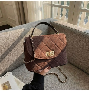 Close-up of brown suede quilted handbag with metal twist lock and chain strap on a sofa