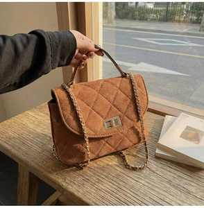 Detail of brown quilted shoulder bag featuring gold twist lock and chain strap on wood
