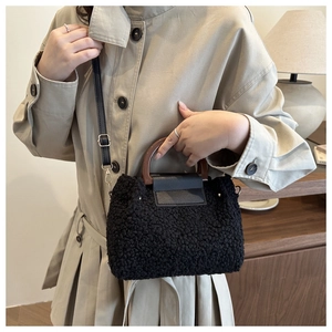 Detail of plush black crossbody bag featuring a curved wooden handle and smooth leather flap