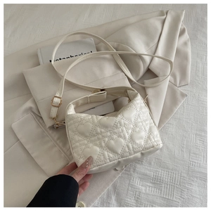 Detail of heart-quilted pattern on cream crossbody bag with golden metal hardware