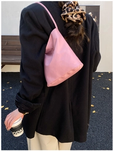 Pink minimalist shoulder bag with unique triangular structure on model in outdoor setting