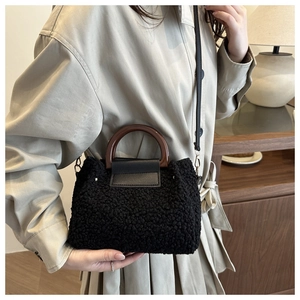 Detail of black faux shearling bucket bag featuring dark brown wood-textured handle