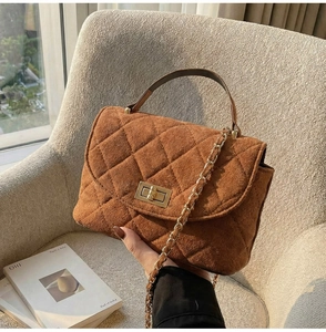 Detail of a brown quilted leather chain bag with metal twist lock on a beige chair