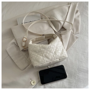 Detailed view of beige heart-quilted PU leather handbag with adjustable strap next to a phone