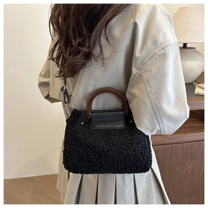 Detail of black plush handbag with wooden circular handle and adjustable crossbody strap