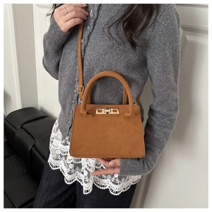 Gros plan d'un sac à main en daim marron avec fermoir doré porté par un mannequin