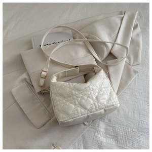 Detail of cream quilted handbag with heart stitching and gold metal hardware on blazer