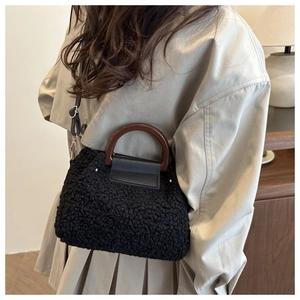 Gros plan du sac seau noir en peluche avec poignée en bois brun et rabat en cuir chic