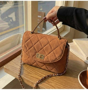 Detail of caramel brown quilted handbag with gold turn-lock and chain strap textures