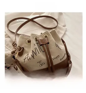 Close-up of cream canvas bucket bag with cherry print and brown leather drawstring detail