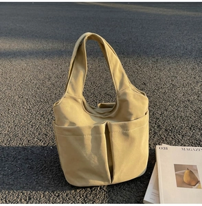 Détail du sac fourre-tout en nylon beige avec plusieurs poches sur sol extérieur