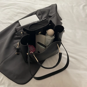 Large black pebbled leather tote bag with gold hardware shown on a grey blazer