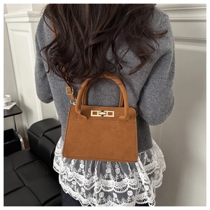 Détail du sac à bandoulière en daim marron avec boucle dorée porté avec un pull gris