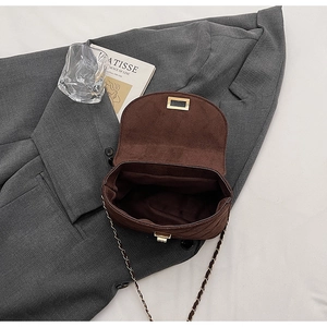 Detail of dark brown suede crossbody bag with gold hardware lock on grey blazer