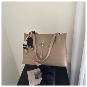 Detail of khaki leather tote bag featuring decorative silk scarf and front zipper pocket