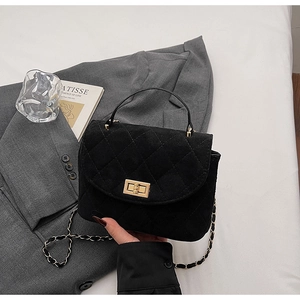 Close-up of black quilted suede bag with a gold lock and chain strap on a blazer