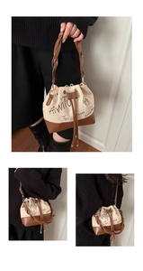 Close-up of suede bucket bag featuring embroidered lettering and woven handle detail