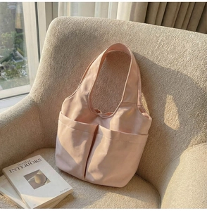 Détail d'un sac seau en nylon rose clair avec grandes poches sur un fauteuil beige doux
