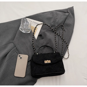 Detail of black quilted leather texture with gold twist lock and chain strap on grey blazer