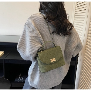 Detail of dark green quilted shoulder bag with gold chain strap worn with a grey sweater