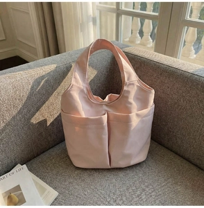 Détail du sac seau en nylon rose clair avec deux poches avant sur un canapé