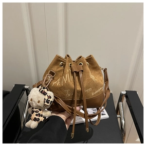 Detail of a brown suede bucket bag with drawstring closure and cute teddy bear pendant