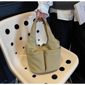 Détail d'un sac seau en nylon vert clair avec deux poches avant sur une chaise blanche