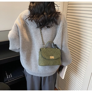 Detail of dark green quilted crossbody bag with golden turn-lock and chain strap