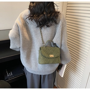 Close-up of dark green quilted suede bag with gold lock and chain strap on a model