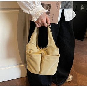Détail d'un sac seau en toile beige avec deux poches avant et des poignées larges