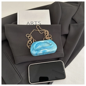 Detailed macro of blue marble acrylic clutch bag with golden chain on grey fabric