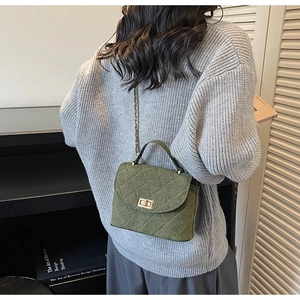Detail of green quilted crossbody bag with gold chain strap on a grey sweater