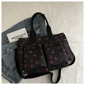 Détail d'un sac cabas en nylon noir à motifs cerises avec plusieurs poches zippées