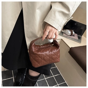 Close-up of brown heart-quilted leather bucket bag held by a model in a modern office set