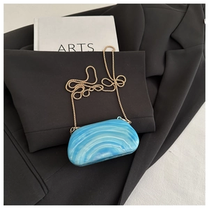Macro shot of blue marble texture evening clutch with elegant gold chain strap