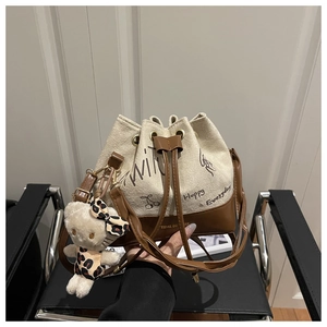 Detail of canvas bucket bag with graffiti print, brown leather trim and plush doll charm