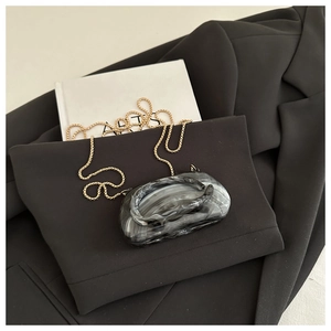 Macro shot of marble textured evening clutch with a golden metal chain on a black suit