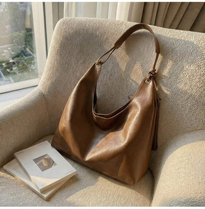 Detail of vintage brown PU leather hobo bag with silver ring buckles on a beige sofa