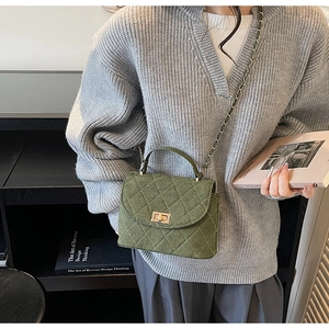 Detail of dark green quilted chain bucket bag on model with gold twist lock closure