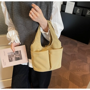 Détail du sac seau jaune moutarde montrant les grandes poches avant et la texture du tissu