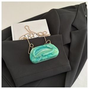 Detail of green marble acrylic evening bag with gold sphere chain on black suit background