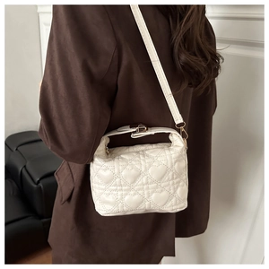 Close-up of white heart-quilted crossbody bag worn with a formal brown blazer jacket