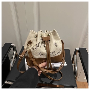 Detail of canvas bucket bag with brown leather trim, drawstring, and cherry print