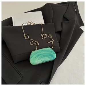Detail of green marble acrylic evening bag with gold chain strap on black blazer